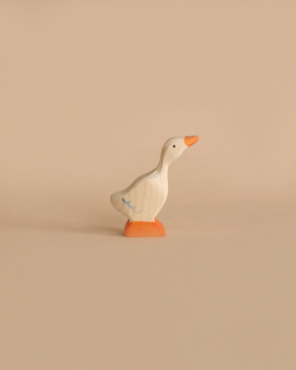 A minimalistic wooden duck figurine stands on a light beige surface against a matching beige background. This Holztiger Goose, Small is painted white with an orange beak and orange feet. Its simple design features a few subtle blue lines on its wings, embodying the charm of handcrafted wood, Made in Europe.