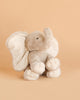 The Bukowski - August Elephant is a soft, light gray plush toy sitting upright on a beige background, featuring large floppy ears, a curved trunk, and embroidered detailing on its feet.
