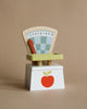 A colorful wooden Market Scale with a fan-like weight indicator numbered from 1 to 10, mounted on a white base featuring a red apple design, perfect for pretend play shopping.