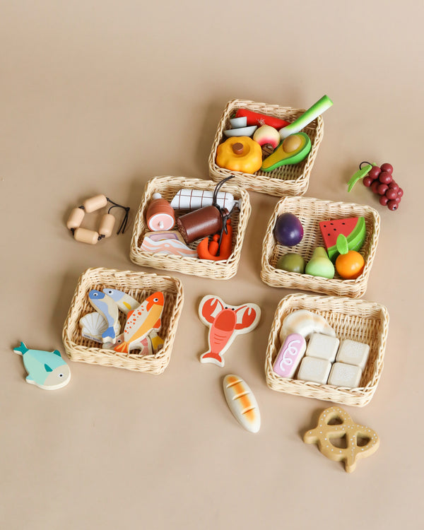 Various wooden toy food items, including fruits, vegetables, and seafood, are neatly arranged in small handcrafted Market Baskets on a beige background.