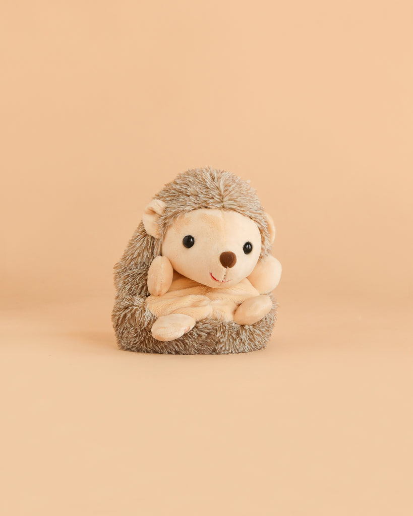 The Bukowski - Sweet Hubert Hedgehog - Sitting features a round face, small black eyes, and a soft tan body; it sits upright against a solid beige background, making it the perfect safe toy companion for nap time.