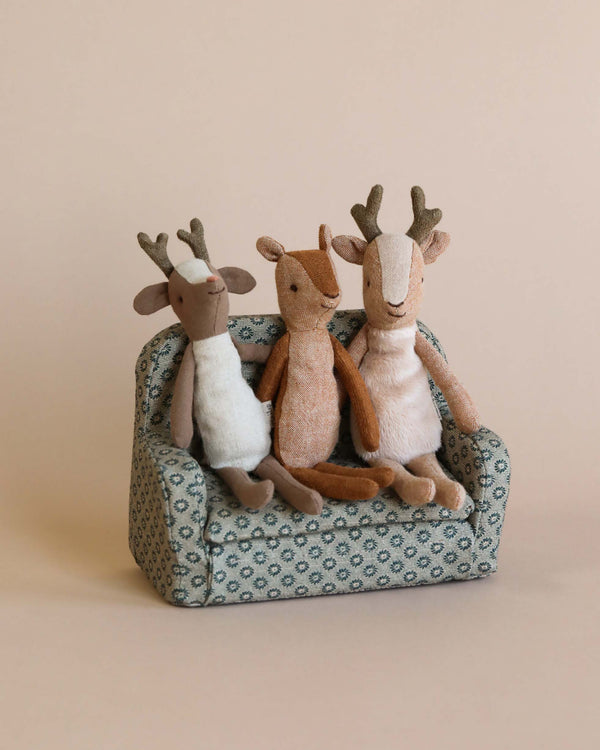Three small deer stuffed animals sitting on a couch together. 