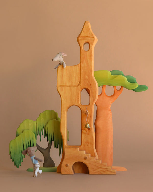 The Ostheimer Fairytale Tower with Maileg Romeo and Juliet Set features two small mice interacting in a wooden castle with colorful trees on a brown backdrop. A bell hangs in the arched doorway, highlighting classic handcrafted charm.