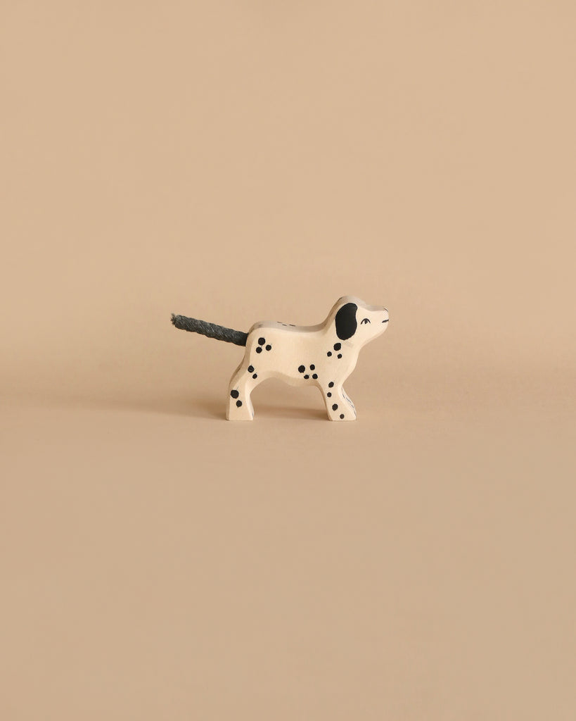 A small, white, Dalmatian-shaped candle with black spots and a black wick for a tail stands on a beige surface, echoing the charming style of the Holztiger Handmade Wooden Farm Animals Set.