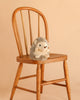 Bukowski - Sweet Hubert Hedgehog - Sitting is a safe stuffed animal, shown sitting on a wooden chair against a plain beige background—perfect as a cozy nap time toy.