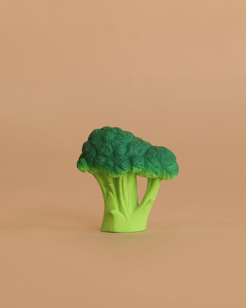 Brucy the Broccoli Teething Toy, a green plastic broccoli floret, sits on a plain light brown background—perfect for teething or sensory play.