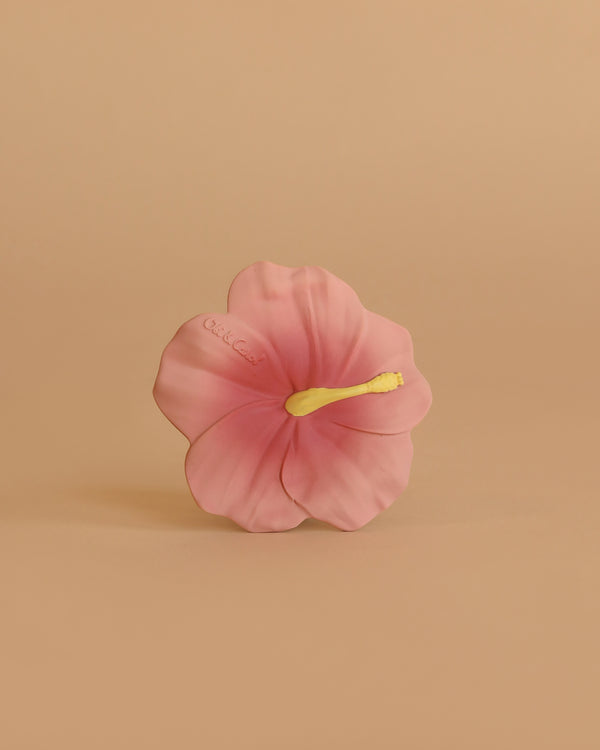 Iris the Hibiscus Teething Toy features a single pink hibiscus flower with a yellow stamen, centered against a plain beige background—an elegant and soothing sensory teether for babies.