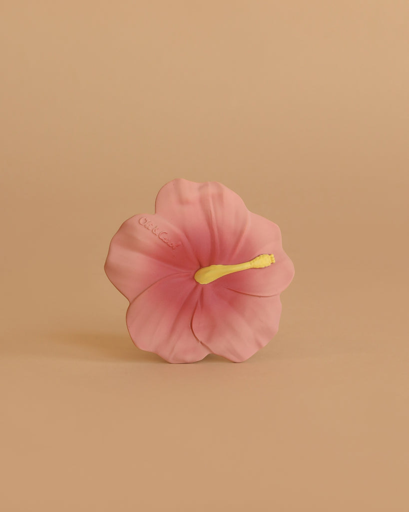 Iris the Hibiscus Teething Toy features a single pink hibiscus flower with a yellow stamen, centered against a plain beige background—an elegant and soothing sensory teether for babies.