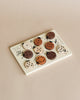 A variety of Wooden Tray Puzzles - Count to 10 Ladybugs with different designs and topping styles are neatly arranged on a rectangular ceramic plate against a beige background.