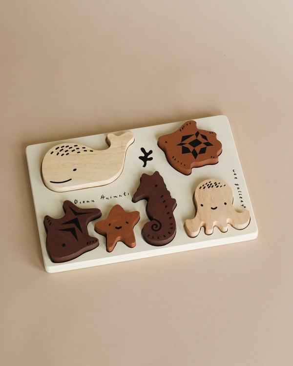 Sentence with Product Name: A Wooden Tray Puzzle - Ocean Animals featuring marine animal shapes including a whale, turtle, starfish, seahorse, and octopus from the ocean set, set against a plain beige background.