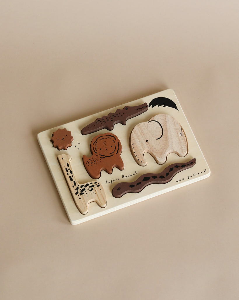 A Wooden Tray Puzzle - Safari Animals on a beige surface featuring various animal shapes like a whale, elephant, and others, each piece labeled with its name.