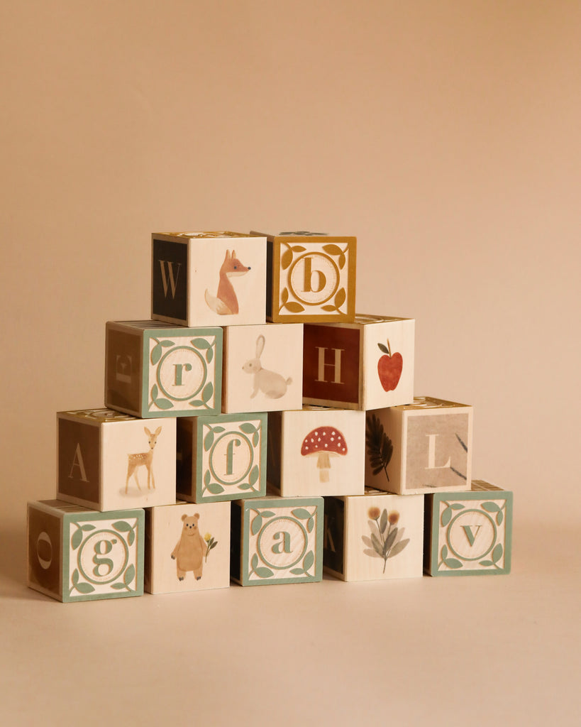 A pyramid of the Newborn Gift Set - Pink blocks, each featuring a letter and illustrations like animals, a mushroom, flower, and strawberry, arranged against a plain beige background.