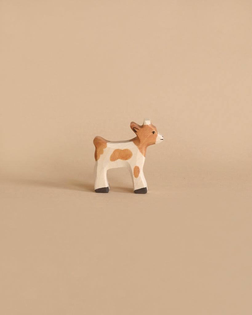 A Holztiger Handmade Wooden Animal Play Set brown and white calf figurine, featuring European craftsmanship, stands on a plain beige background.