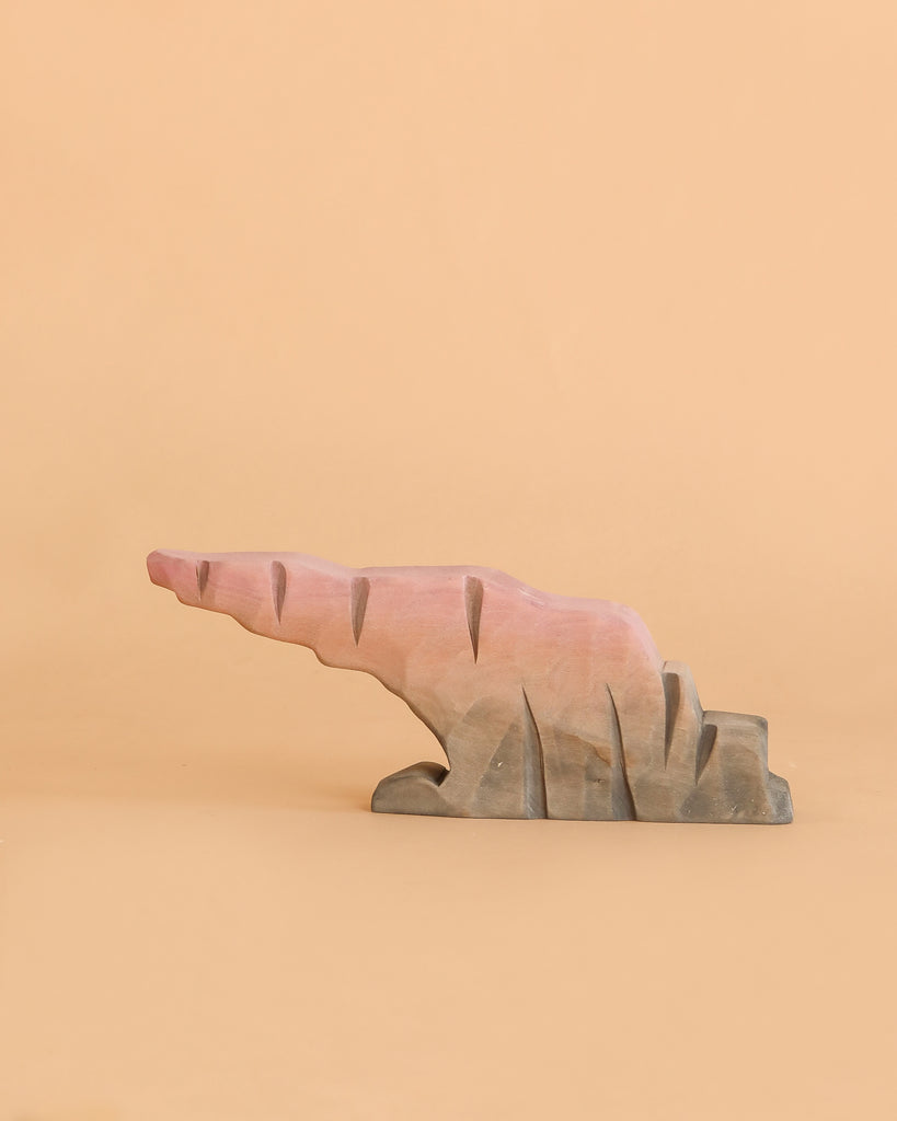 A painted wooden sculpture from the Bumbu Howling Wolf Set, shaped like an abstract rock formation in pink and gray tones, sits on a plain beige background—perfect for imaginative play and crafted from sustainably sourced wood.
