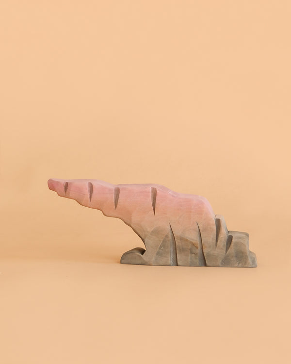 A Bumbu Handmade Wooden Howl Stone, painted in pink and brown hues, mimics an abstract, jagged rock formation against a plain beige background—inviting imaginative play and capturing the whimsical spirit of a Howlstone toy.
