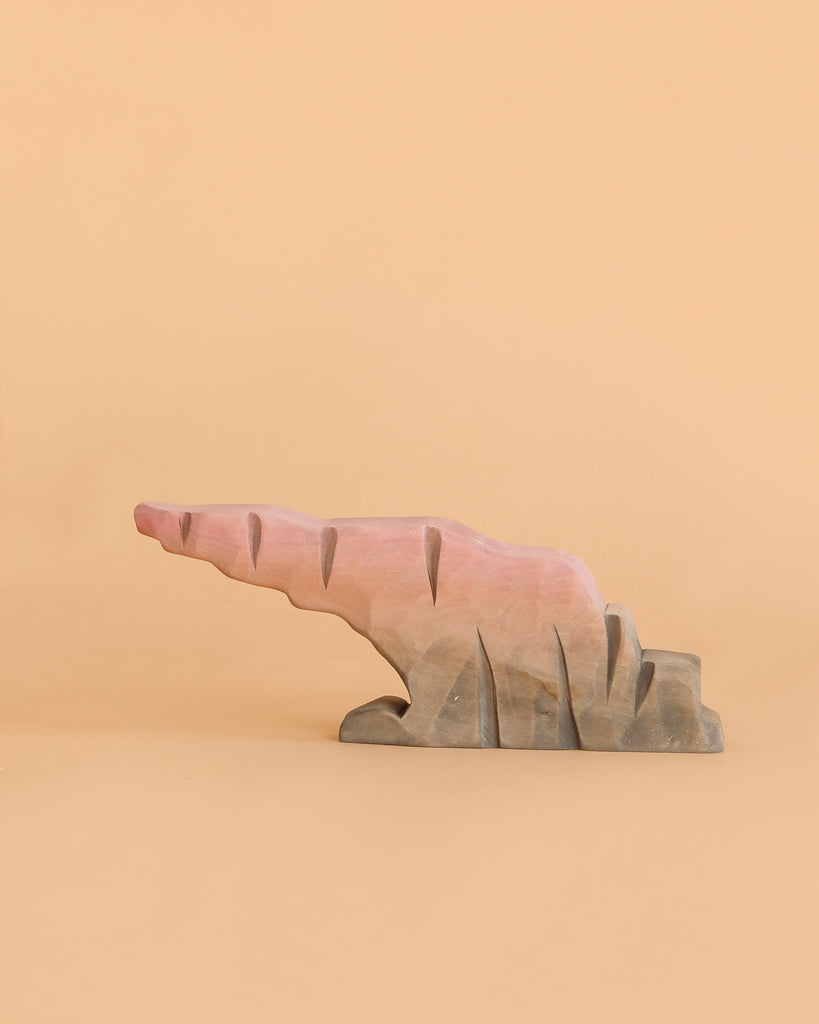 A Bumbu Handmade Wooden Howl Stone, painted in pink and brown hues, mimics an abstract, jagged rock formation against a plain beige background—inviting imaginative play and capturing the whimsical spirit of a Howlstone toy.