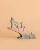 The Bumbu Howling Wolf Set features two carved wooden wolves—one large and one small—standing atop a pink and gray rock formation against a plain beige background. Crafted from sustainably sourced wood, this set of toys inspires imaginative play and brings a touch of wild beauty to any space.