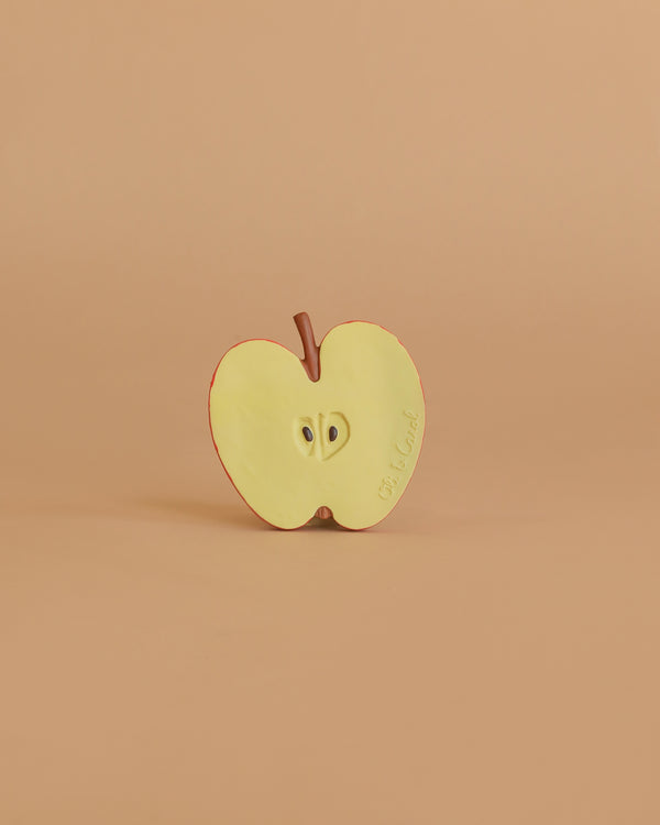 Pepita the Apple Teething Toy is a realistic, halved apple made from natural rubber, shown upright on a beige background with visible seeds and stem—ideal for baby teething and sensory play.