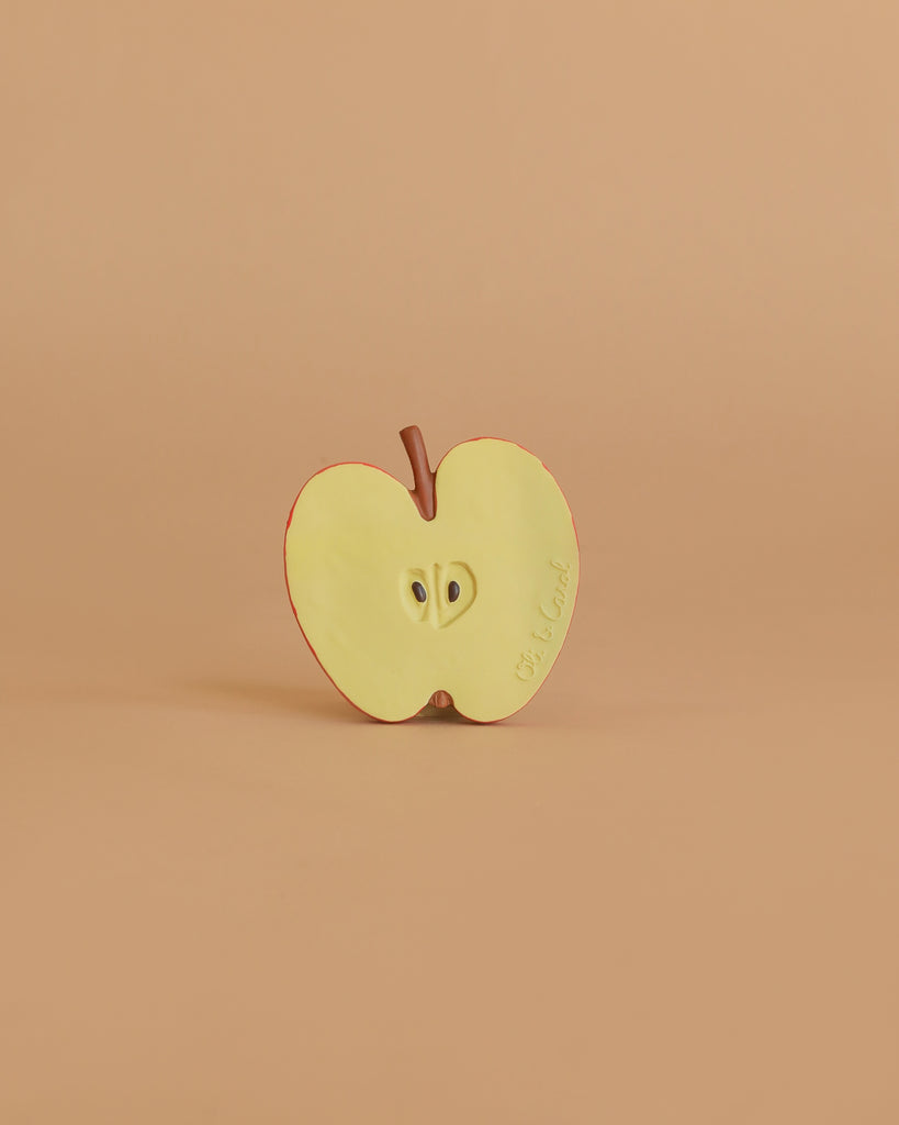 Pepita the Apple Teething Toy is a realistic, halved apple made from natural rubber, shown upright on a beige background with visible seeds and stem—ideal for baby teething and sensory play.