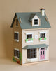 A detailed model of the Foxtail Villa Dollhouse with a pink front door, window boxes with flowers, and decorative elements like a small tree and a "home sweet home" sign.