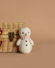 The Cuddle + Kind Baby Snowman - Candy Cane, featuring a red and white striped scarf, stands by a wicker basket on a beige background—an ideal collectible plush for stuffed animal fans.