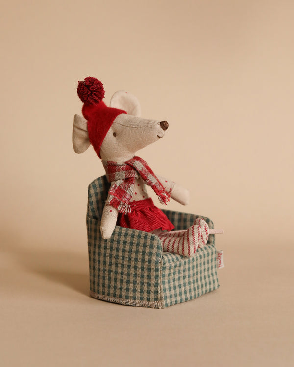 The Maileg Christmas Mouse - Big Sister is charmingly dressed in a red sweater, striped scarf, and matching hat, sitting on a tiny green checkered armchair against a plain background.