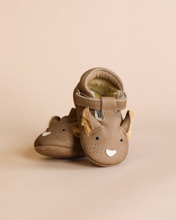 A pair of adorable brown Donsje Leather Spark Exclusive Lined Shoes styled with cute fox faces, featuring pointy ears and white accents for the eyes and mouth, handmade from premium leather, displayed against a soft beige background.