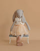 The Maileg Bunny, Size 3 - Classic - Ballet Suit and Skirt - Cream, sits on a small white bench in a peach tulle skirt, sequin vest, and ballet slippers against a plain beige background.