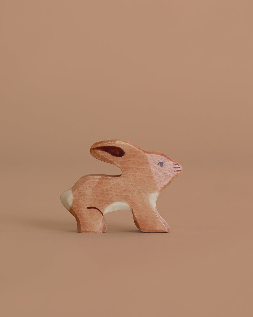 The Holztiger Handmade Wooden Woodland Animals Set includes a small, handcrafted wooden rabbit figurine with brown and white painted details, ideal for open-ended play, displayed against a plain light brown background.