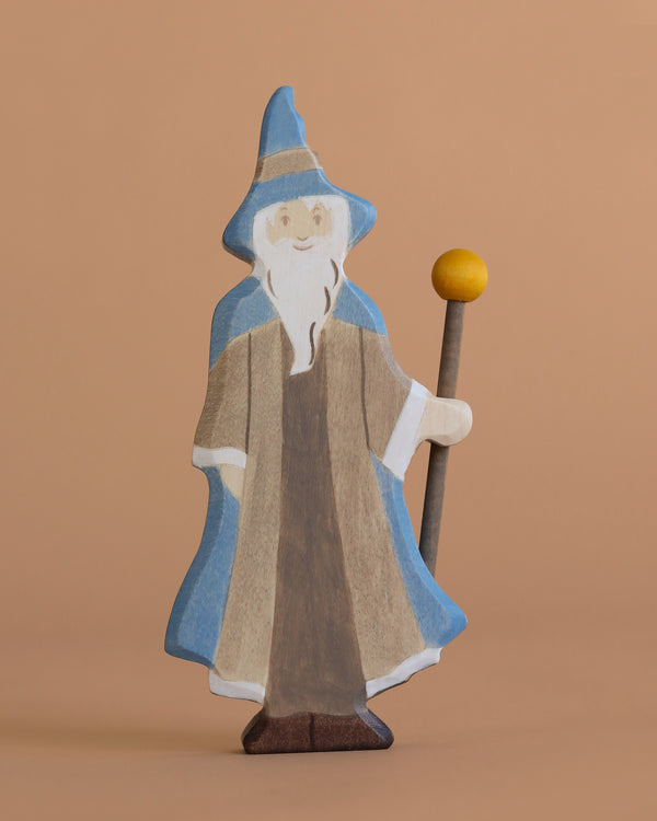The Holztiger Magician is a handcrafted wooden figure featuring a long white beard, blue hat and cloak, brown robe, and a staff with a yellow sphere—perfect for imaginative play on any plain beige background.