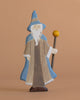 The Holztiger Magician is a handcrafted wooden figure featuring a long white beard, blue hat and cloak, brown robe, and a staff with a yellow sphere—perfect for imaginative play on any plain beige background.
