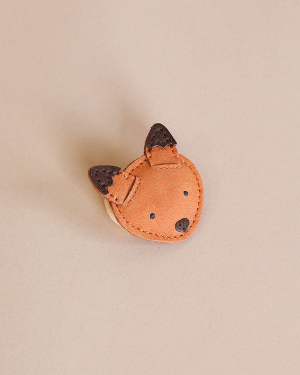 A small, handmade fairtrade Donsje Leather Hair Tie - Fox keychain with dark brown accents for the ears and nose, displayed on a light beige background.
