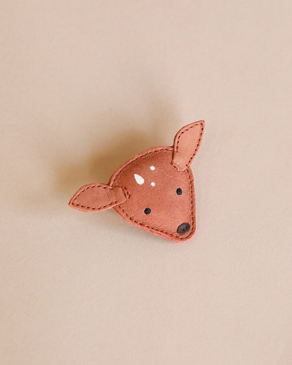 A handmade fairtrade Donsje Leather Hair Tie - Deer with white spots and stitched details, displayed on a light beige background.