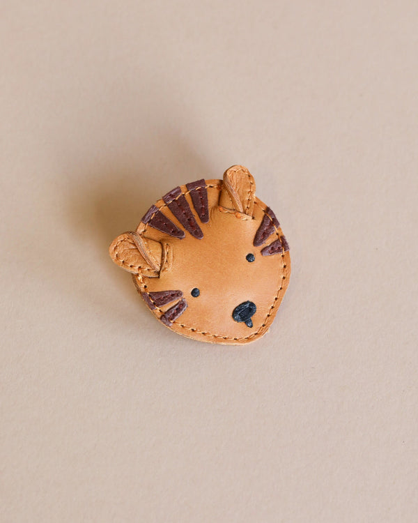 A Donsje Leather Hair Tie - Tiger shaped like a tiger's face, featuring stitched stripes and details, displayed on a plain beige background.