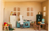 A toy mouse dressed as a chef stands by a blue stove in a charming miniature vintage kitchen, surrounded by dollhouse furniture, food items, and kitchenware, with two windows on the back wall—making the Maileg Fully Furnished Dollhouse Set + Gift With Purchase (Restock Expected In August) perfect for any Maileg or miniature dollhouse display.