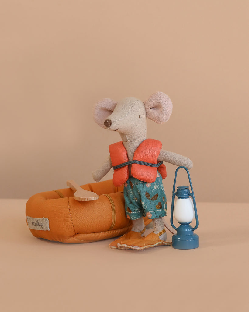 The Maileg Big Brother Mouse Holiday Adventure Set features a mouse in a life jacket, blue floral shorts, and flippers, alongside a miniature lantern and orange rubber boat with paddle on a plain beige background.