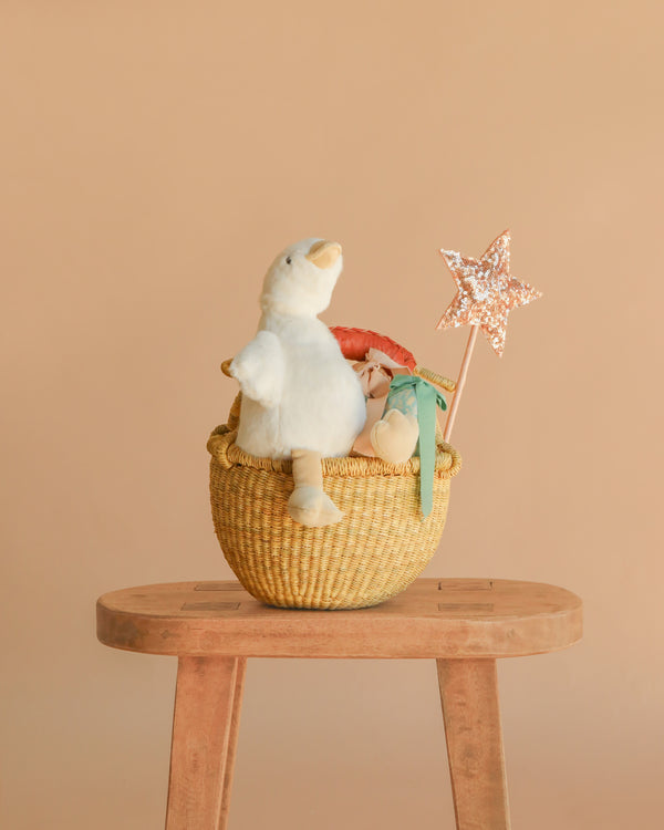 The Easter Basket Gift Set features a woven basket with a white plush goose, plush orange carrot, magic sequin wand, and green ribbon on a wooden stool—perfect for Snuggle Bunnies or Maileg Easter Egg gifts.