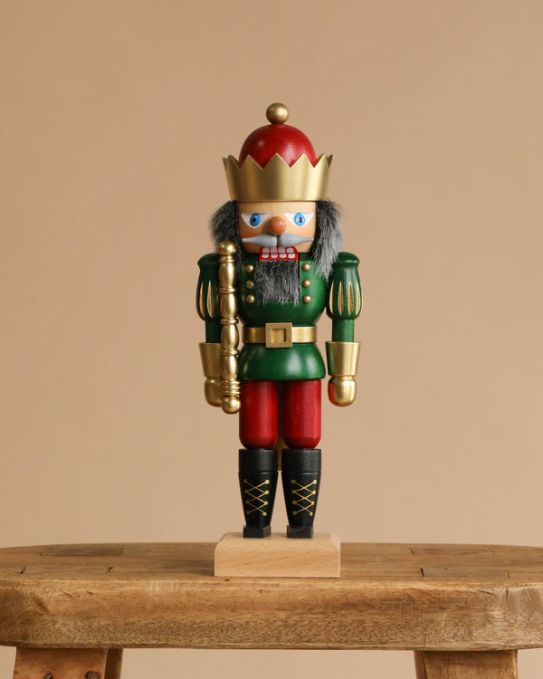 The Christian Ulbricht Collectible Wooden Nutcracker – King (Red and Green) features a gold crown, gray hair, and a red and green uniform, standing on a small wooden bench against a plain beige background.