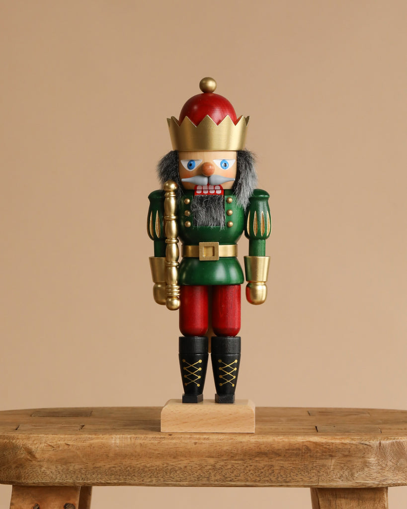 The Christian Ulbricht Collectible Wooden Nutcracker – King (Red and Green) features a gold crown, gray hair, and a red and green uniform, standing on a small wooden bench against a plain beige background.