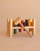 A Rainbow Pound -a- Peg wooden Montessori toy bench with red, yellow, blue, green, and orange pegs and a wooden mallet resting on top, set against a plain beige background. This eco-friendly toy encourages colorful play and learning.