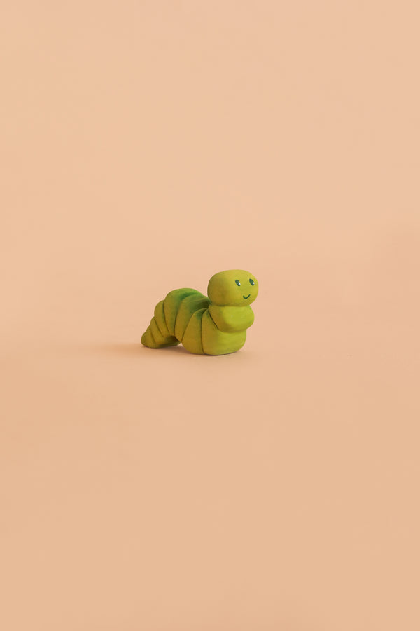 A small, green Bumbu Handmade Wooden Caterpillar with a cute, smiling face sits on a plain peach background, evoking the charm of a Montessori toy perfect for imaginative play.