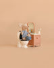 A Maileg LouiMax Bathroom Set features a mouse in a striped shirt and shorts sitting on a toilet beside a charming sink dresser with mirror, toothbrushes, and toothpaste, all set against a plain beige background.