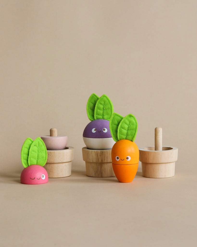 A photograph of four cute wooden toy vegetables with smiley faces. The vegetables include an orange carrot, a purple beet, a pink radish, and a second pink radish lying down. With green felt leaves and small wooden cups against a beige background, these Stacking Wooden Veggies are perfect for budding gardeners.
