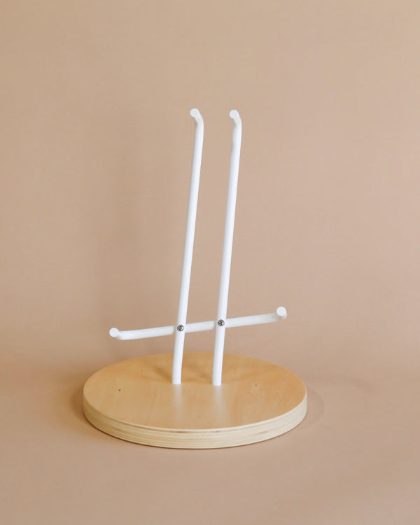 A minimalist wooden jewelry stand with two vertical white bars attached to a circular base, set against a plain beige background, also suitable for displaying Guitar Stand For Loog Mini.