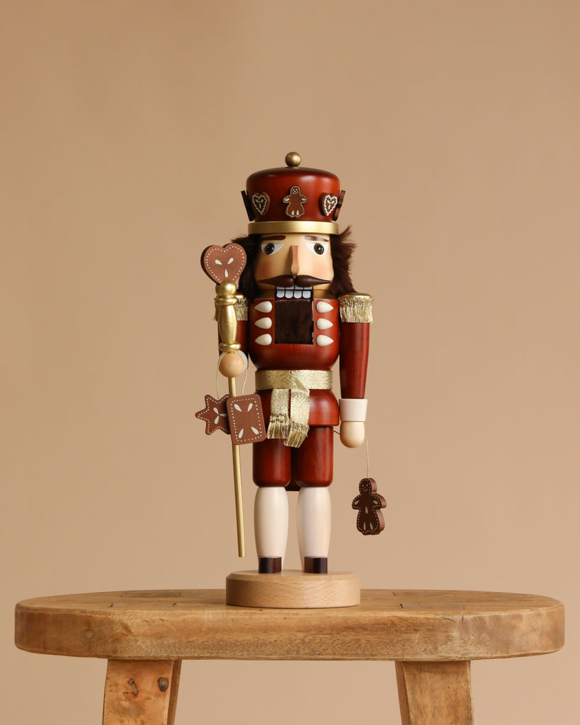 The Christian Ulbricht Collectible Wooden Nutcracker Gingerbread King (Natural) stands 15 inches tall, crafted from solid wood in Germany, holding a staff with a heart-shaped top and a gingerbread figure, set against a plain beige background.