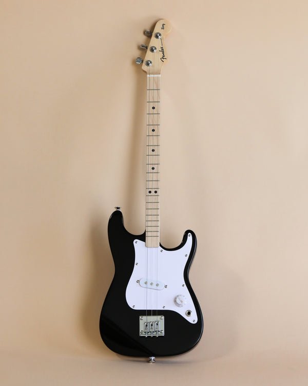 A black 3-string Fender X Loog Stratocaster electric guitar with a white pickguard, positioned vertically against a plain beige background. The guitar has a maple neck and headstock.