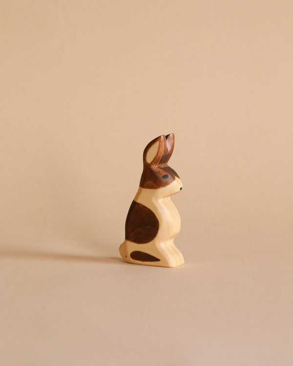 A Handmade Holzwald Standing Spotted Rabbit with dark brown patches on a light beige background. The figurine is intricately carved, showing distinct details and contours, ideal for imaginative play.