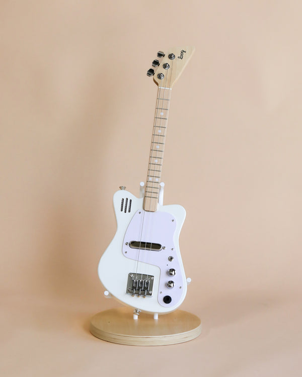 A white 3-string Electric Guitar With Strap stands upright on a rotating display stand against a light beige background. The guitar has a classic design with a glossy finish.