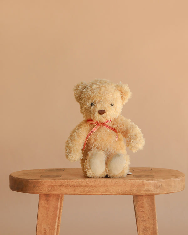 Snuggle Bunnies - Arthur the Bear, featuring a red stripe bow, sits on a wooden stool against a beige background—an ideal nursery companion or thoughtful children’s gift.
