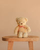 Snuggle Bunnies - Arthur the Bear, featuring a red stripe bow, sits on a wooden stool against a beige background—an ideal nursery companion or thoughtful children’s gift.